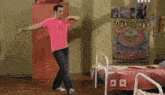 a man in a pink shirt is dancing in a bedroom next to two beds .