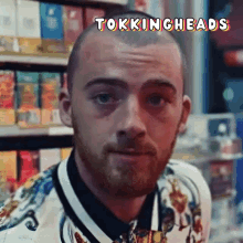 a man with a beard is standing in front of a shelf of cigarettes with the words tokingheads above him