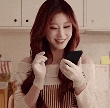 a woman wearing gloves is smiling while holding a cell phone