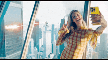 a woman in a plaid shirt is taking a selfie in front of a window