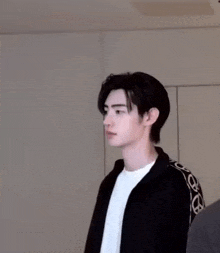 a young man is wearing a black jacket and a white shirt .