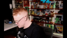a man wearing glasses and a black shirt is sitting in front of a shelf filled with toys