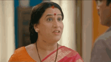 a woman in a pink saree is talking to a man in a room and making a funny face .