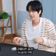 a man in a striped sweater is sitting at a table with the words is up to 118 on the screen