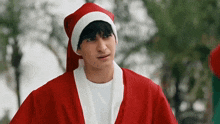 a young man in a santa suit and hat is making a funny face .