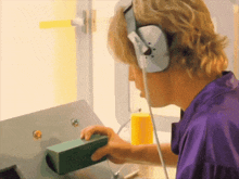 a man wearing headphones and a purple shirt holds a green box