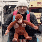a man is holding a stuffed monkey in his arms while standing in front of a big bus .