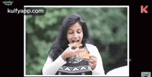 a woman is eating a slice of pizza with the website kulfyapp.com at the bottom of the screen