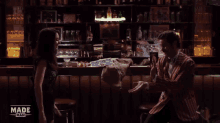 a girl is jumping in the air while another girl sits at a desk with made man written on the bottom right