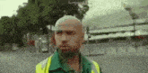 a bald man wearing a green shirt and a yellow vest is standing in a parking lot .