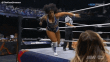 a woman in a wrestling ring is jumping in the air while a referee looks on .