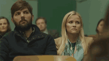 a man and a woman are sitting in a classroom with a group of people .