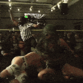 a woman with green hair is kneeling down next to a man in a wrestling ring while a referee watches