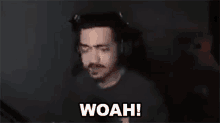 a man wearing headphones is standing in front of a microphone and says woah .