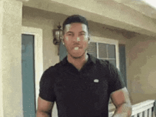 a man in a black shirt is standing in front of a house with a cigarette in his mouth .