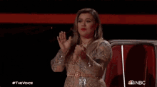 a woman in a sequined dress is sitting in a chair with her mouth open and her hands in the air .