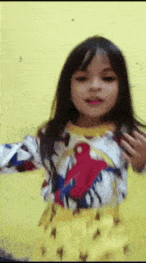 a little girl wearing a shirt with a parrot on it is standing in front of a yellow wall .