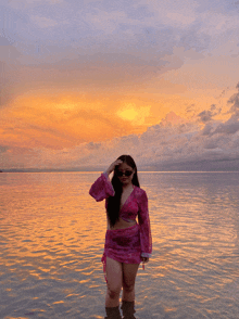 a woman in a pink top and skirt stands in the water at sunset