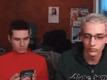 two young men are sitting in a room looking at their phones .