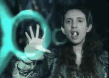 a man with long hair holds up his hand in front of a blue circle