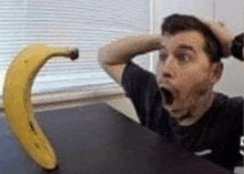 a man is sitting at a table with his mouth open and a banana on it .