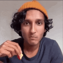 a man with curly hair wearing an orange beanie is eating a piece of food