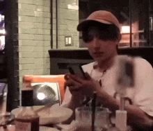 a man in a hat is sitting at a table looking at his cell phone .