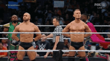 two wrestlers are standing in a wrestling ring with a referee .