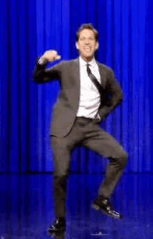 a man in a suit and tie is dancing on stage in front of a blue curtain