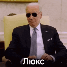 a man in a suit and tie is sitting in a chair wearing sunglasses and making a funny face .