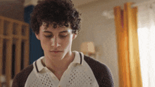 a young man with curly hair is wearing a white and brown sweater