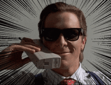 a man wearing sunglasses and a tie is talking on a phone