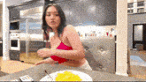 a woman in a red bra is sitting at a table with a plate of food on it .