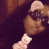 a woman wearing sunglasses and holding a teddy bear is taking a selfie .