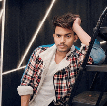 a young man in a plaid shirt is leaning on a staircase