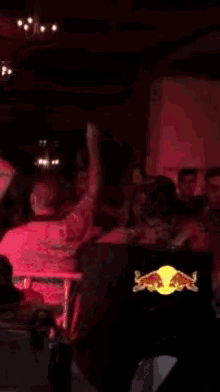 a crowd of people are dancing in a dark room with a red bull logo