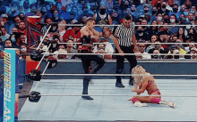 a wrestler is kicking another wrestler in a wrestling ring while a referee looks on