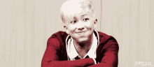 a young man with white hair is making a funny face while sitting with his arms crossed .
