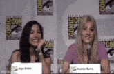 two women are sitting at a table at a comic con