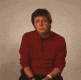 a man in a red sweater is sitting in front of a white wall and making a funny face .