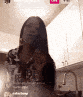 a woman is standing in a kitchen with a live button on her phone