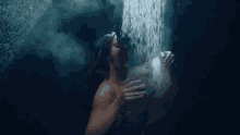 a man is taking a shower in a dark room with water falling on his face .