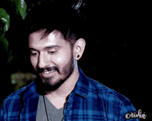 a man with a beard wearing a blue plaid shirt is smiling and has the name anisha on the bottom