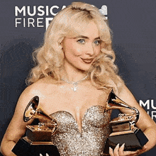a woman in a dress is holding two grammy awards