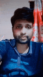 a man with a beard is standing in front of a red curtain and looking at the camera .