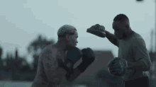 two men are boxing in a park and one of them is wearing gloves .