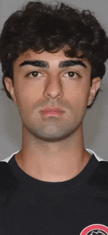 a young man with curly hair and a tattoo on his face is wearing a black shirt .