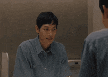 a man in a blue shirt looks at himself in the mirror