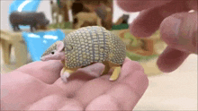 a small armadillo toy is being held in a person 's hand .