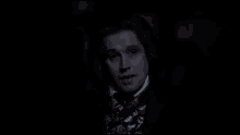 a man in a suit and tie is standing in the dark .